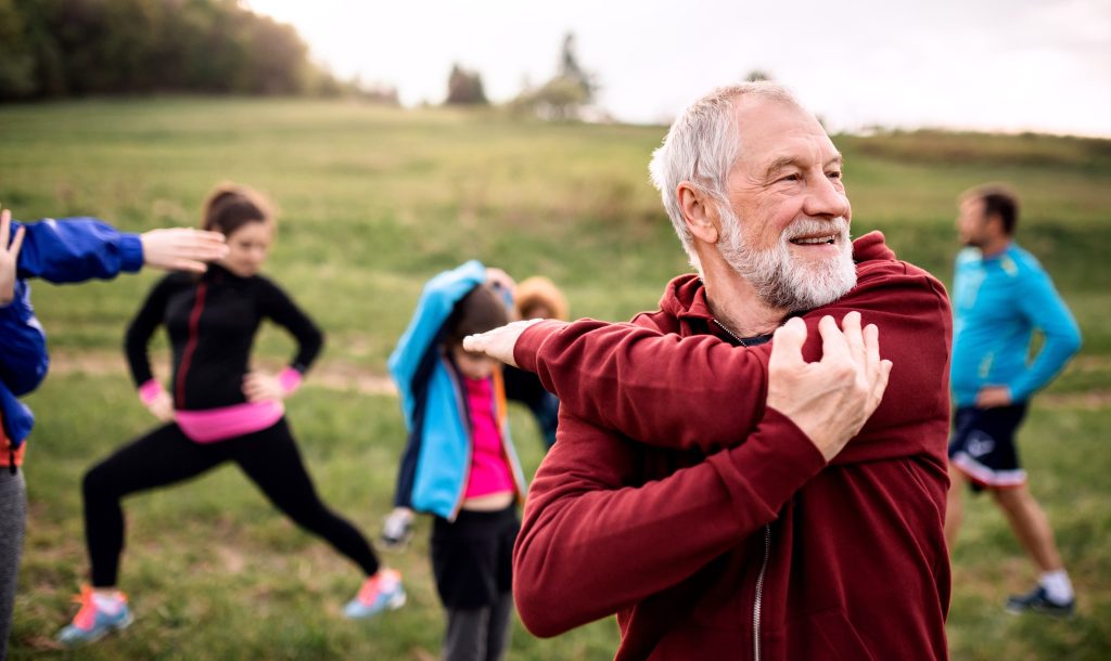 Older adult stretching outdoors with a community exercise group